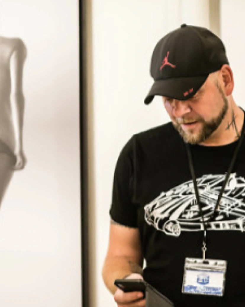 Jocelyn Bouget sur son stand, casquette noire et badge d'exposant, devant l'un de ses tableaux
